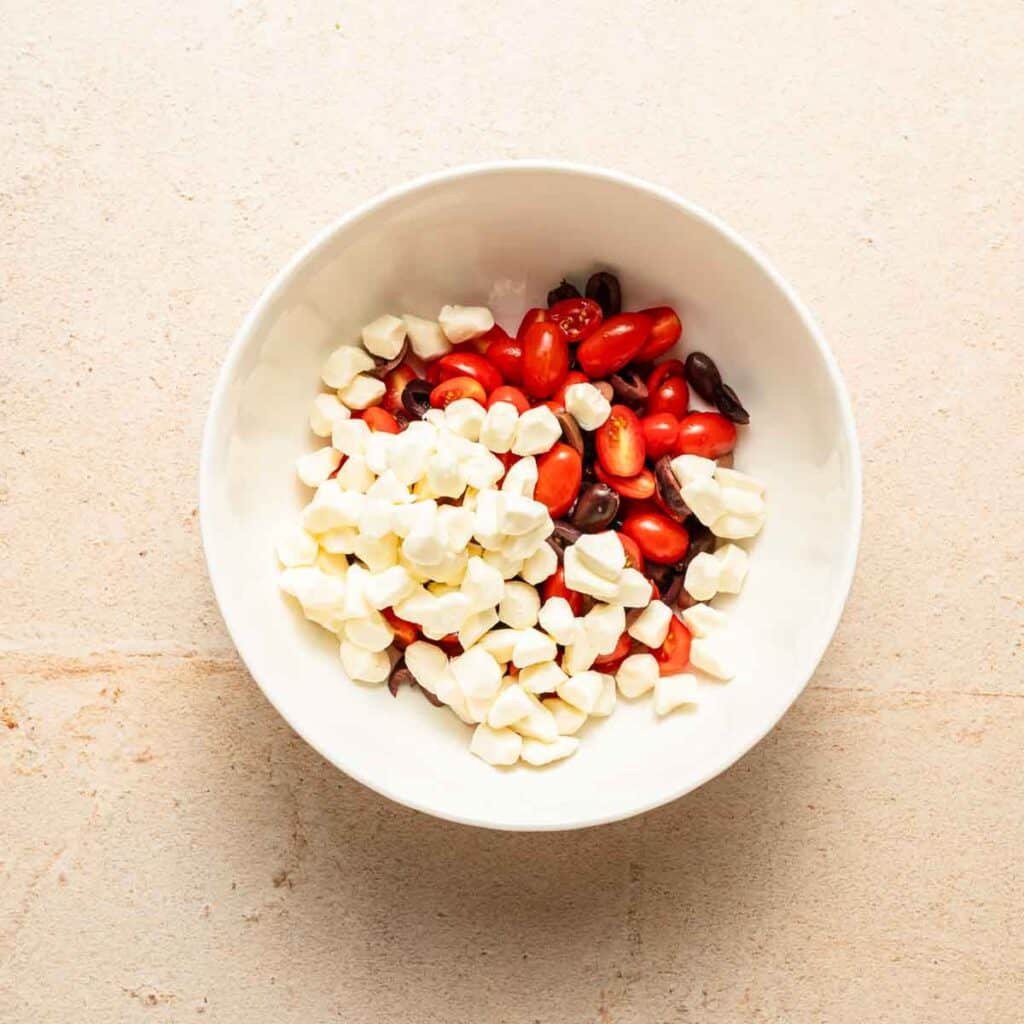 fresh mozzarella pearls, sliced grape tomatoes and sliced olives in a large white bowl.