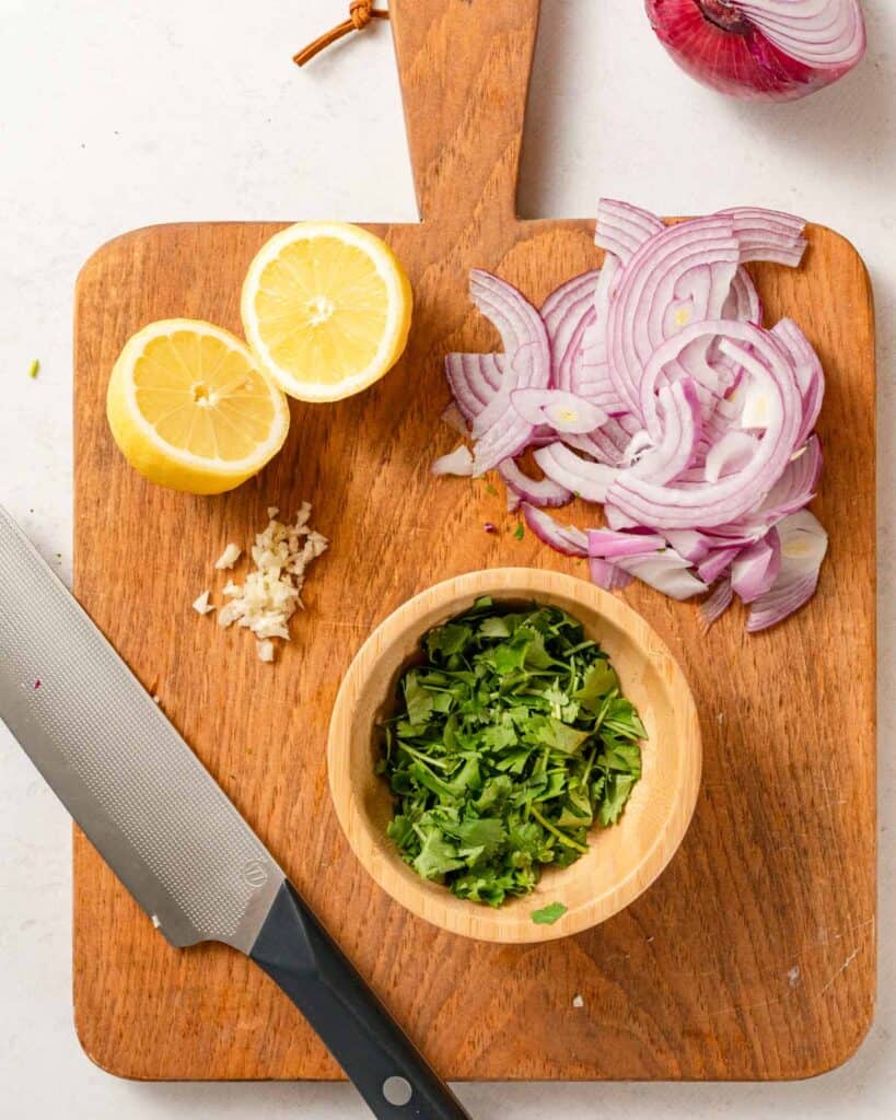 cut cilantro in bowl on cutting board with lemon garlic and sliced onion on the side.