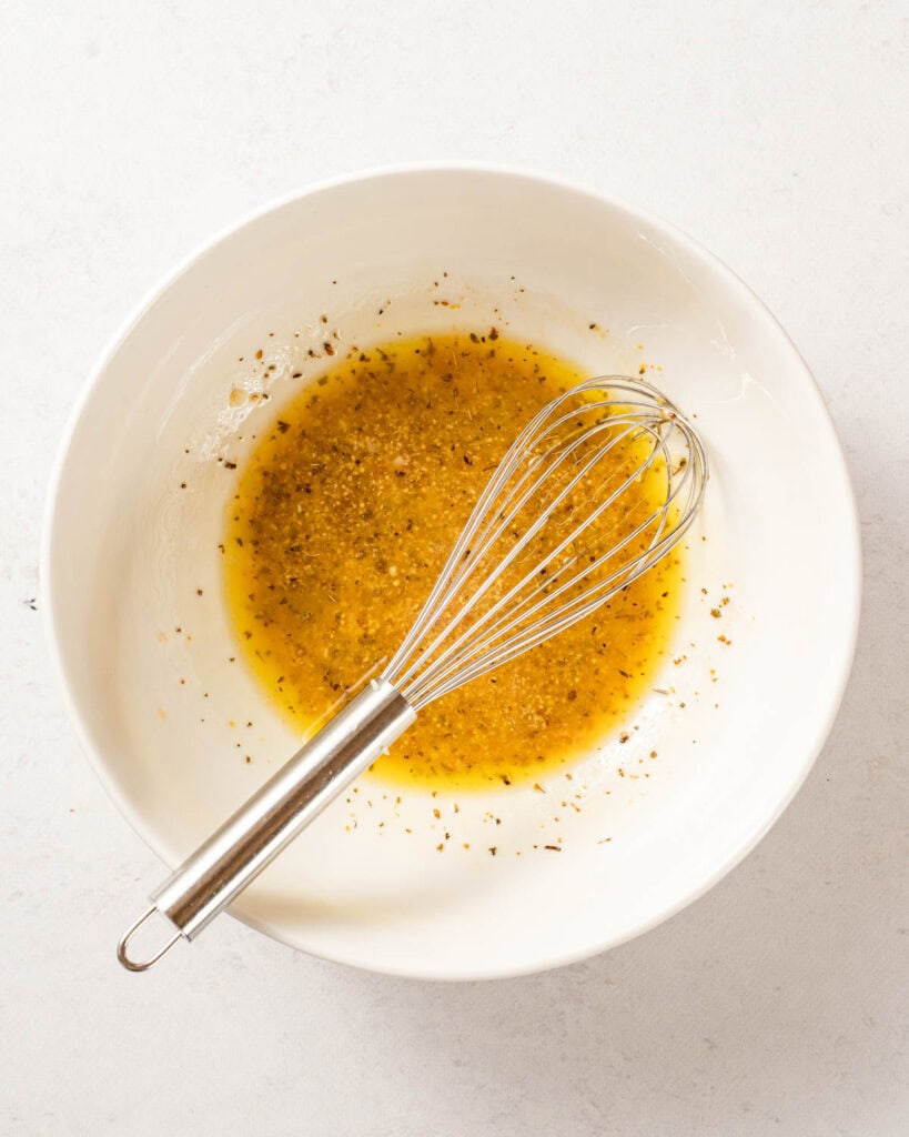 dressing in white bowl with whisk.