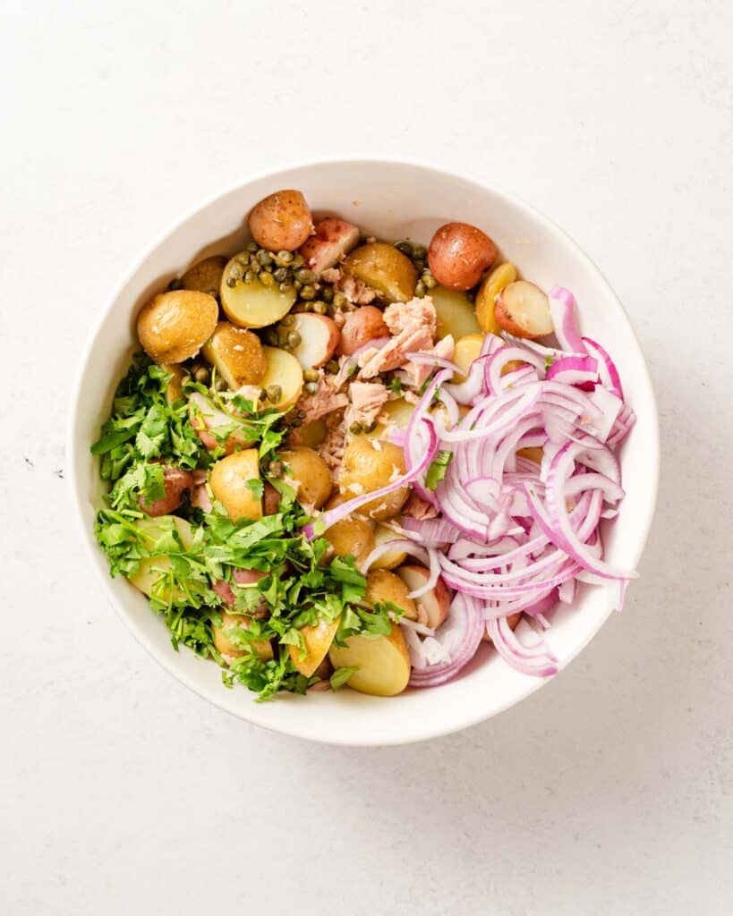 potatoes herbs tuna and sliced onion in white bowl.