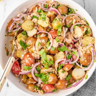 tuna and potato salad in white bowl with spoon.