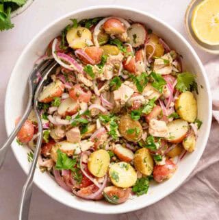 potato and tuna salad in white bowl with serving spoons.