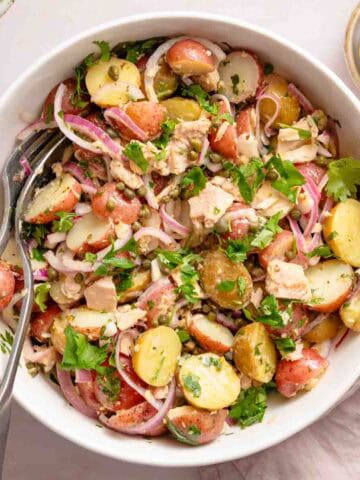 potato and tuna salad in white bowl with serving spoons.