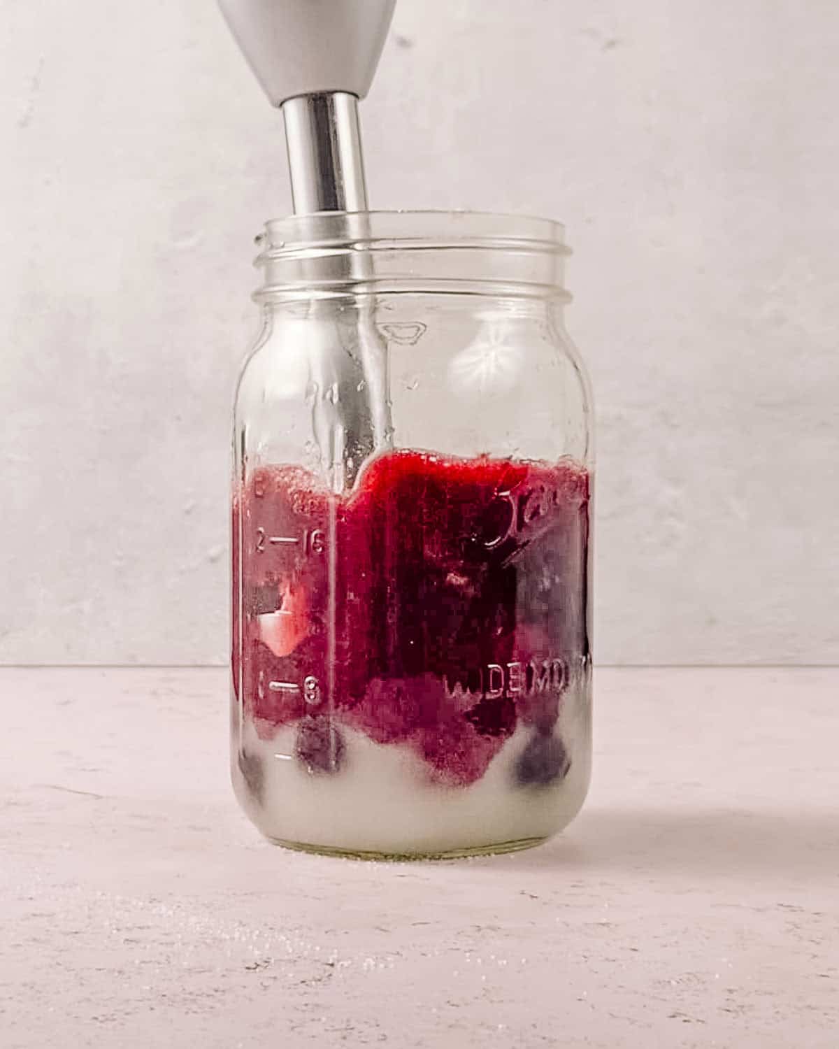 cherry juice water and sugar being blended in a jar with an immersion blender.