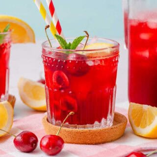 cherry lemonade in glass with two straws and cherry garnishes.