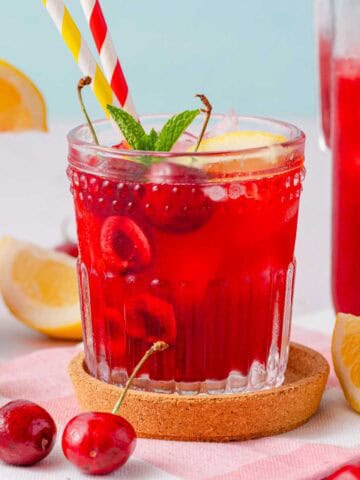 cherry lemonade in glass with two straws and cherry garnishes.