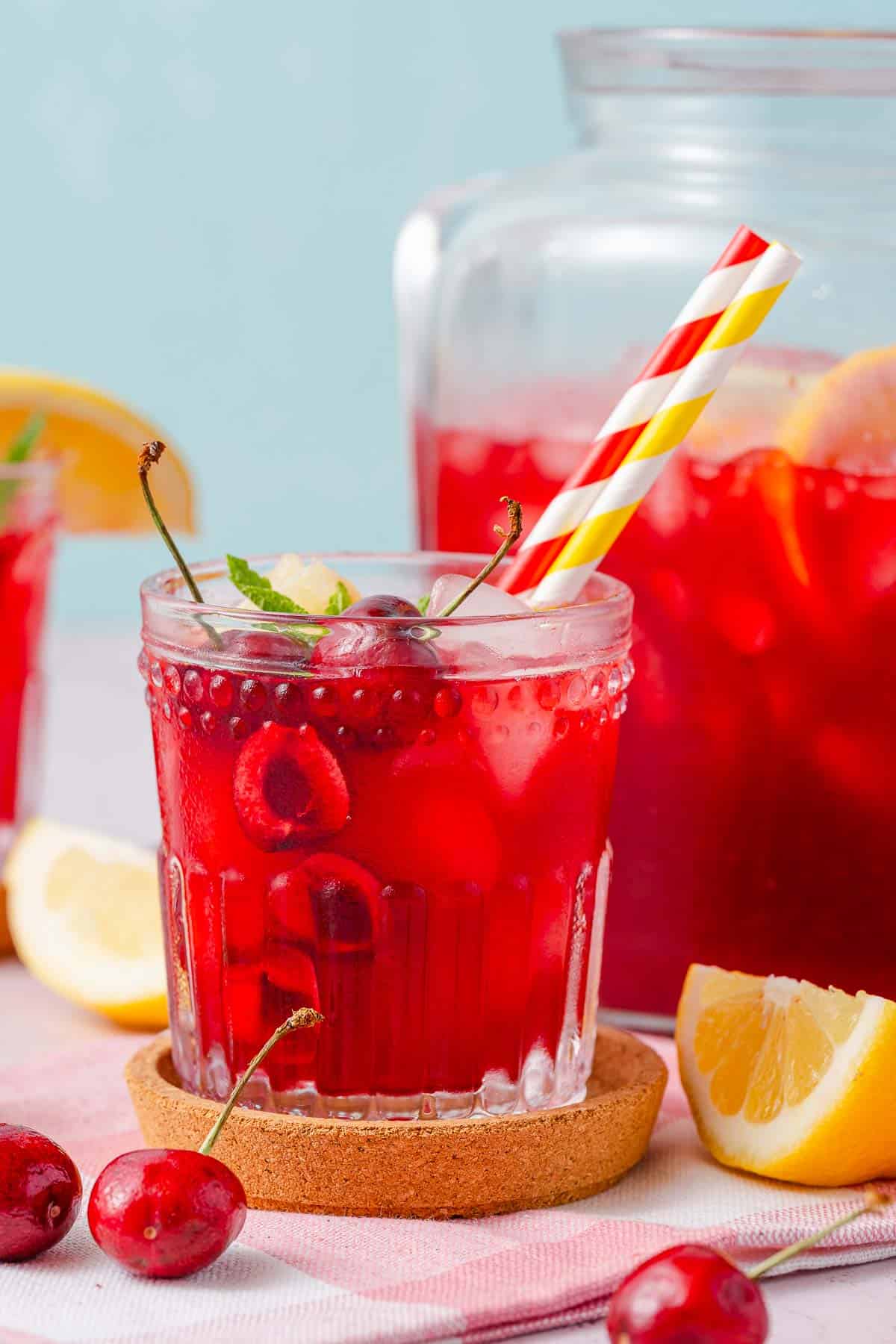 cherry lemonade in pitcher and glass with lemon and cherry garnishes.