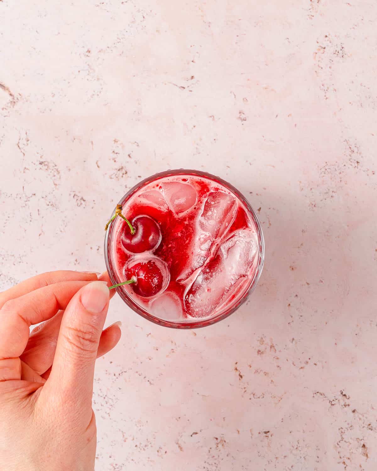 glass of cherry juice being garnished with a fresh cherry.