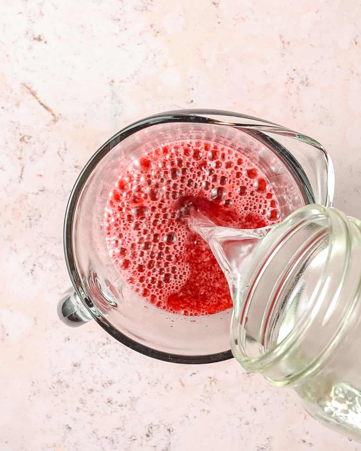 water being poured into a pitcher with cherry juice inside.