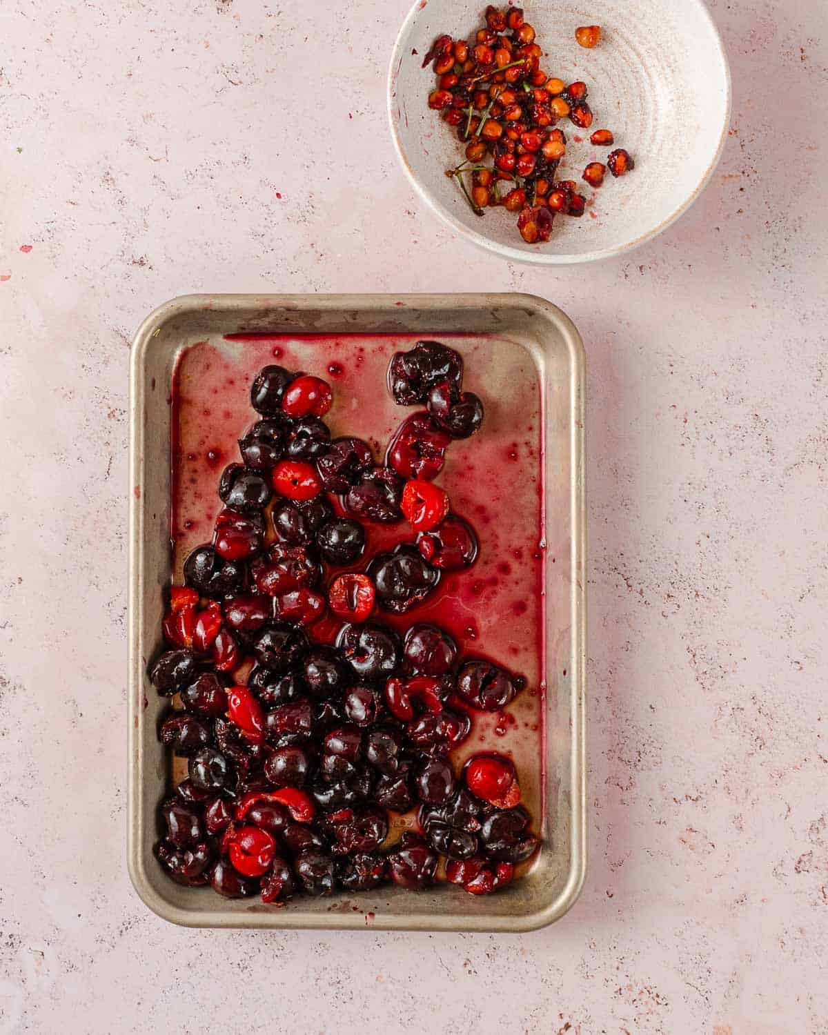 tray of pitted cherries with bowl of pits on the side.