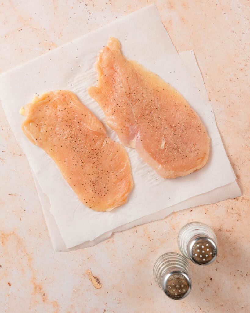 thin-sliced chicken breasts on parchment paper with salt and pepper shakers on the side.