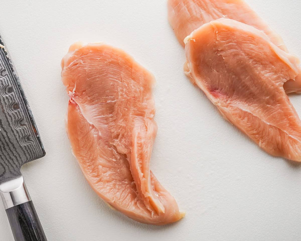 three pieces of thin sliced chicken breast with a knife on the side.