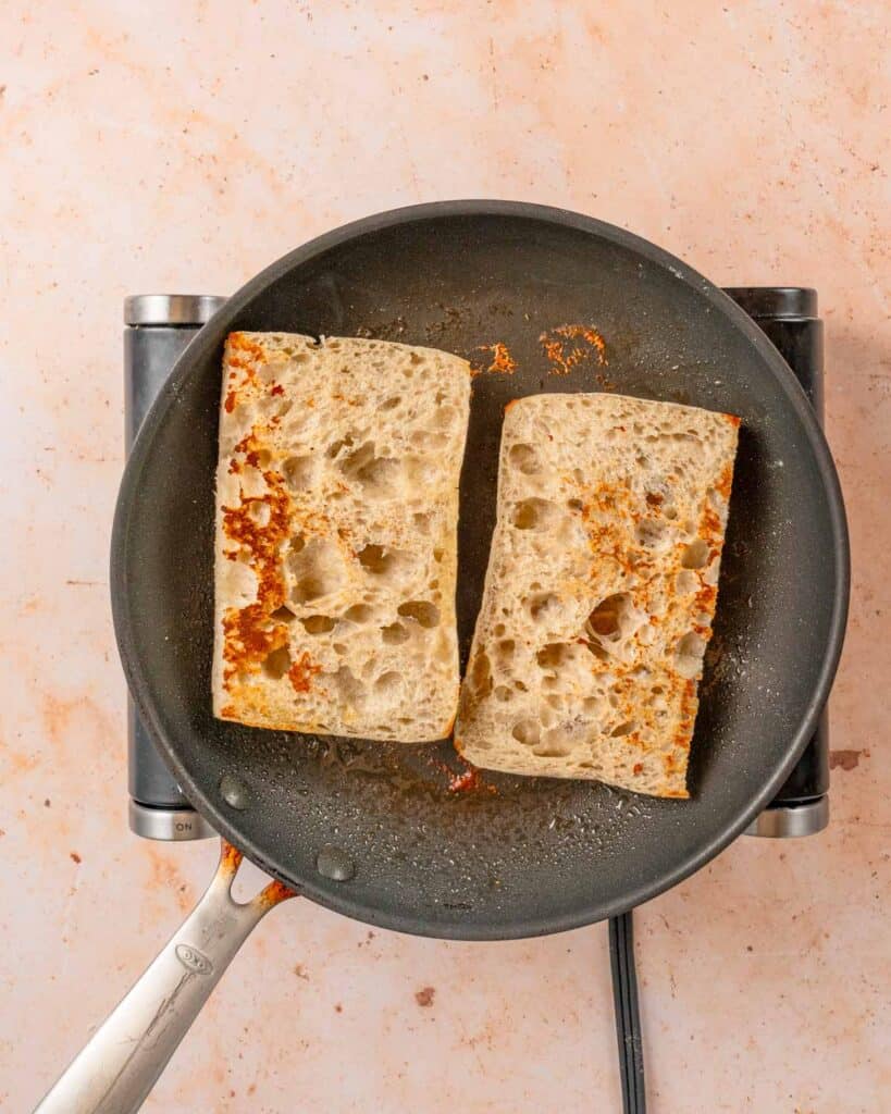 two pieces of ciabatta bread browned in skillet.