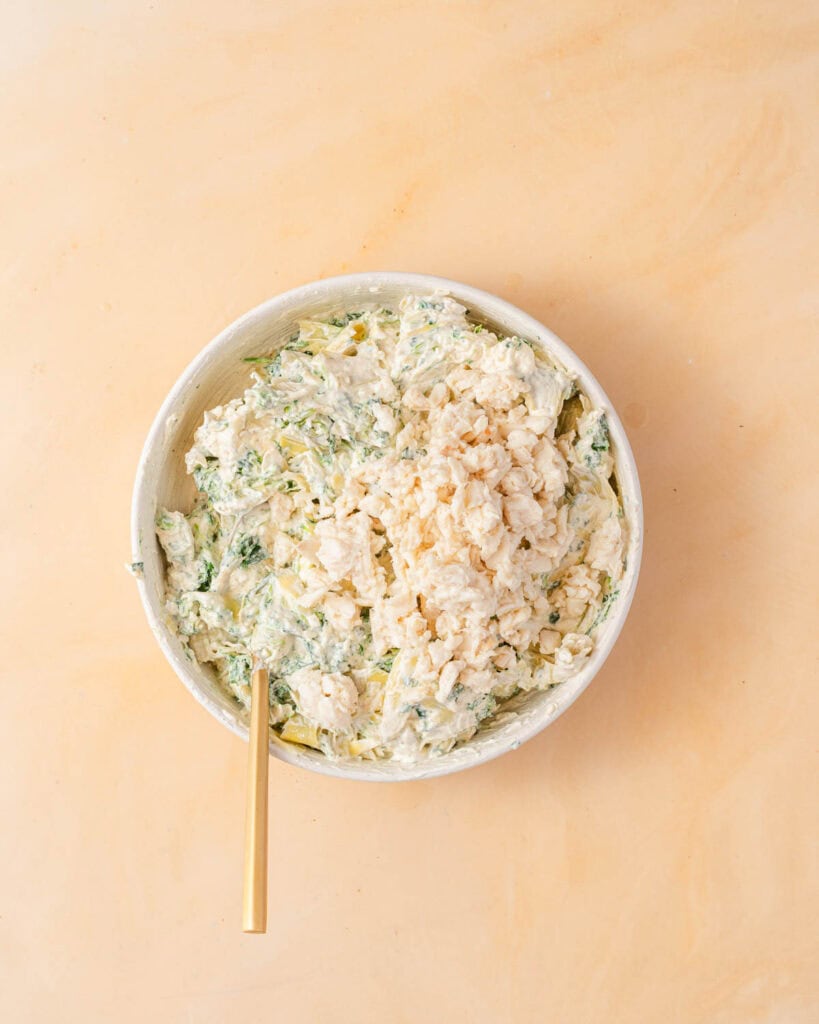 crab meat on top of spinach artichoke dip in bowl.