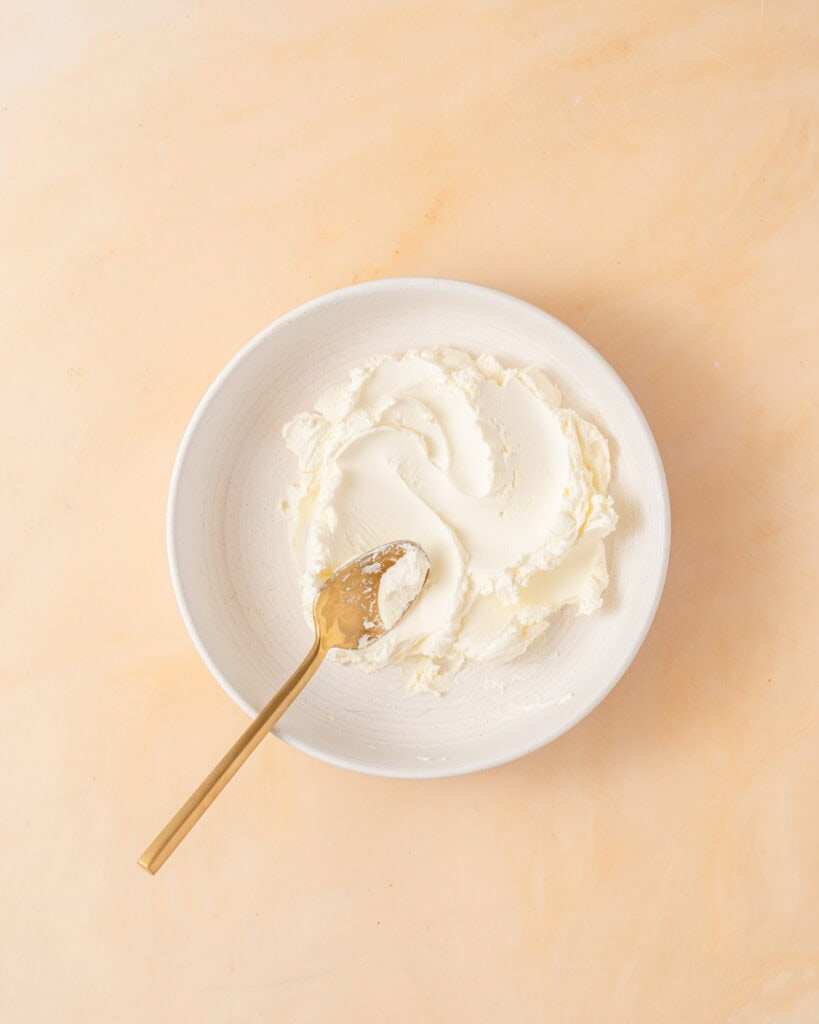 cream cheese stirred in a bowl with a wooden spoon.