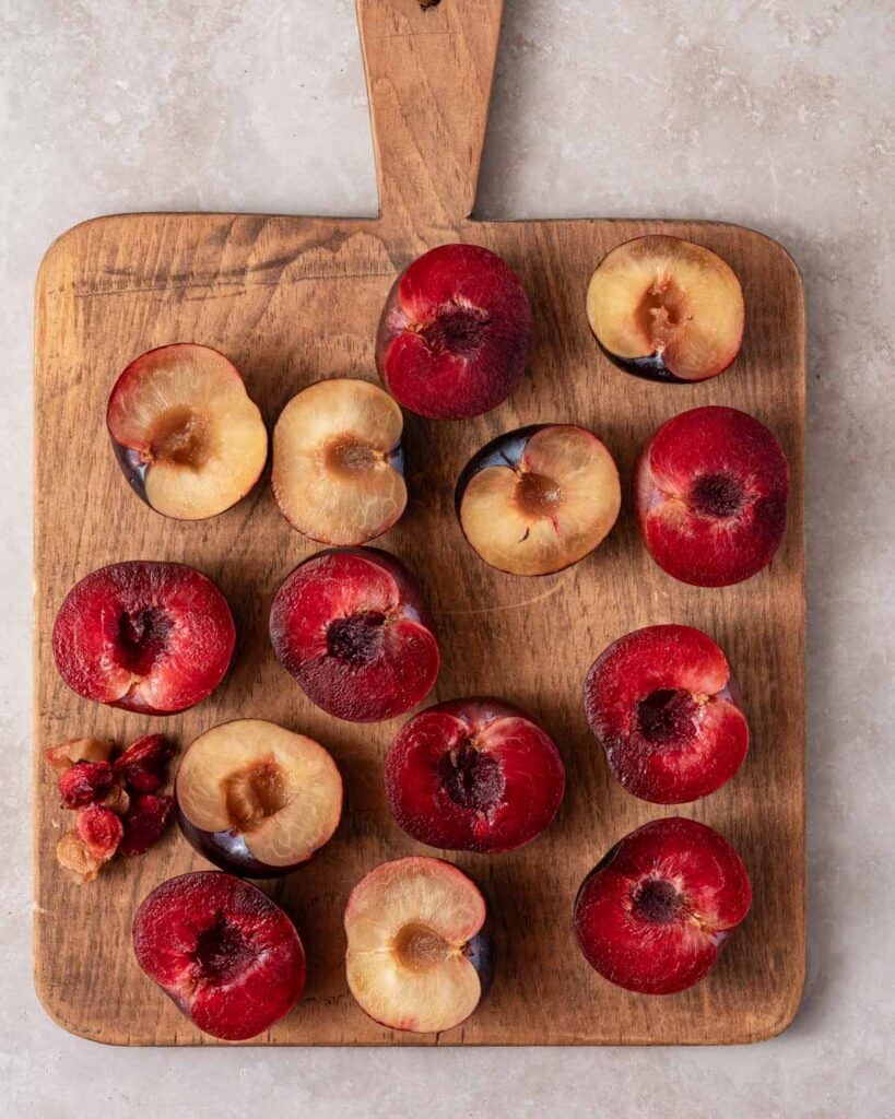 cut fresh plums on wooden cutting board with stones removed.
