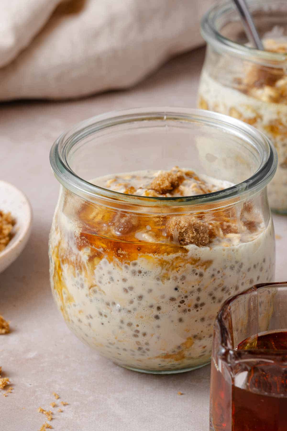 oats in glass jar topped with maple syrup and brown sugar.
