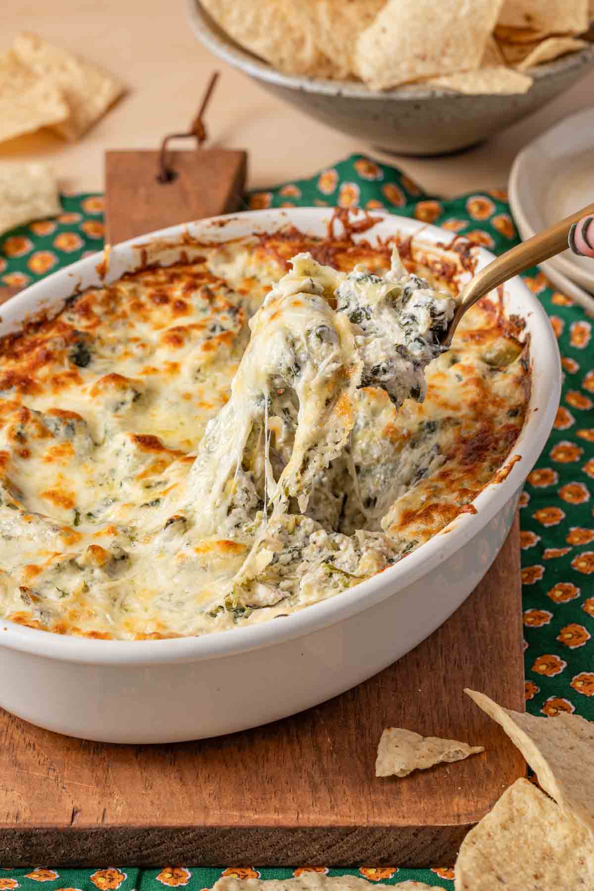 dish of crab spinach artichoke heart dip with cheesy top being scooped out with a spoon.
