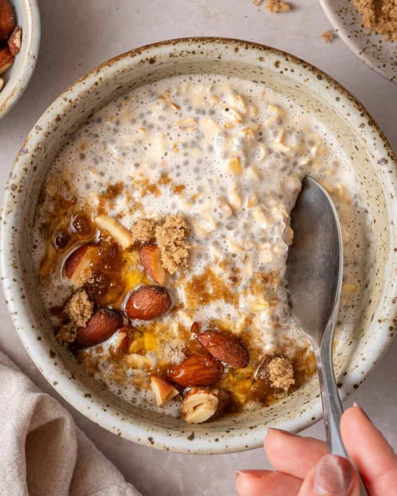 oats topped with brown sugar maple syrup and nuts being spooned out of bowl.