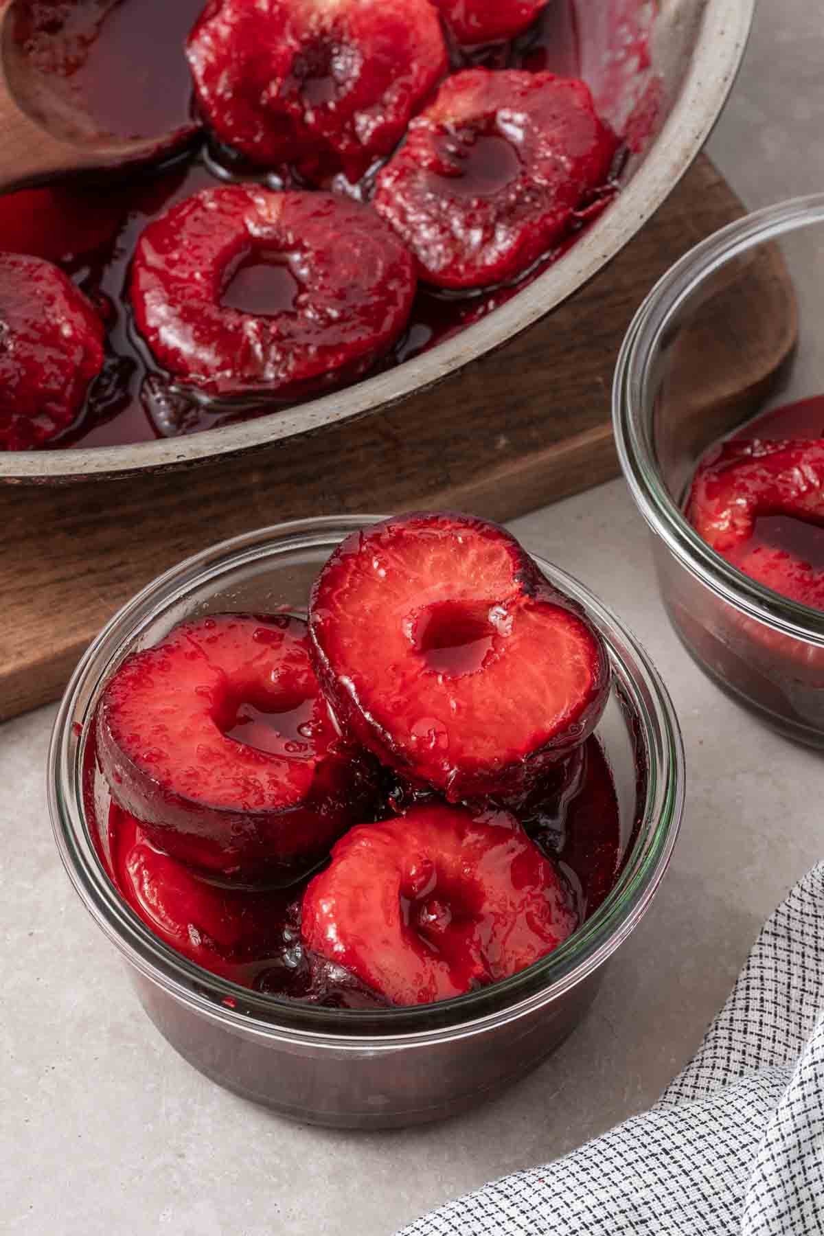 stewed plums in glass jar with pan of plums on the side.