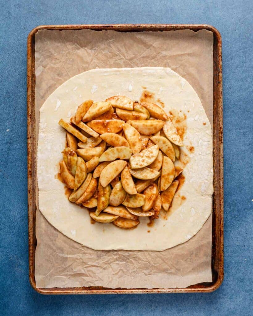 apple filling in the center of a sheet of puff pastry on a baking tray.