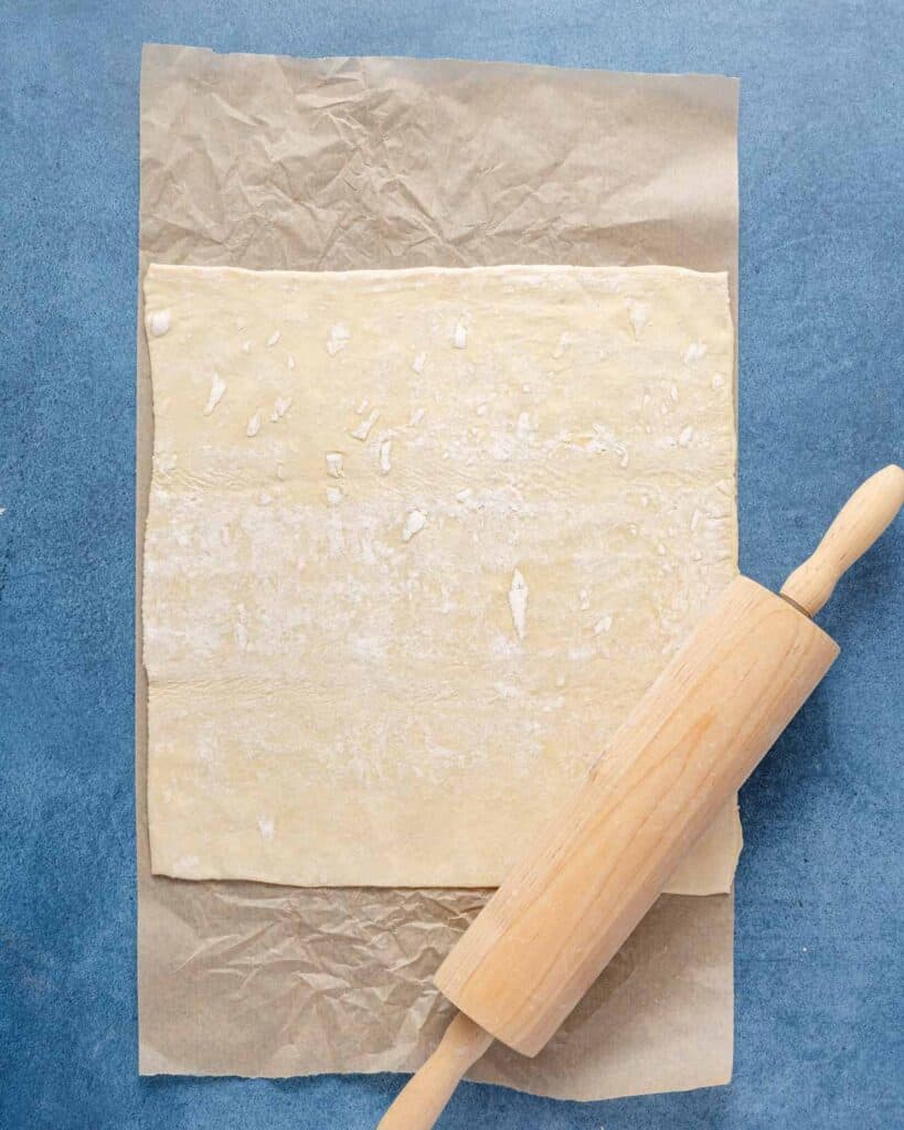 puff pastry on parchment paper with rolling pin on the side.