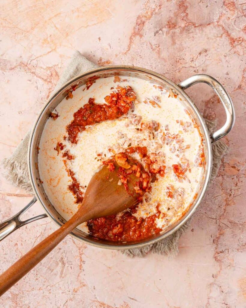 tomato sauce and cream in pan with wooden spoon.