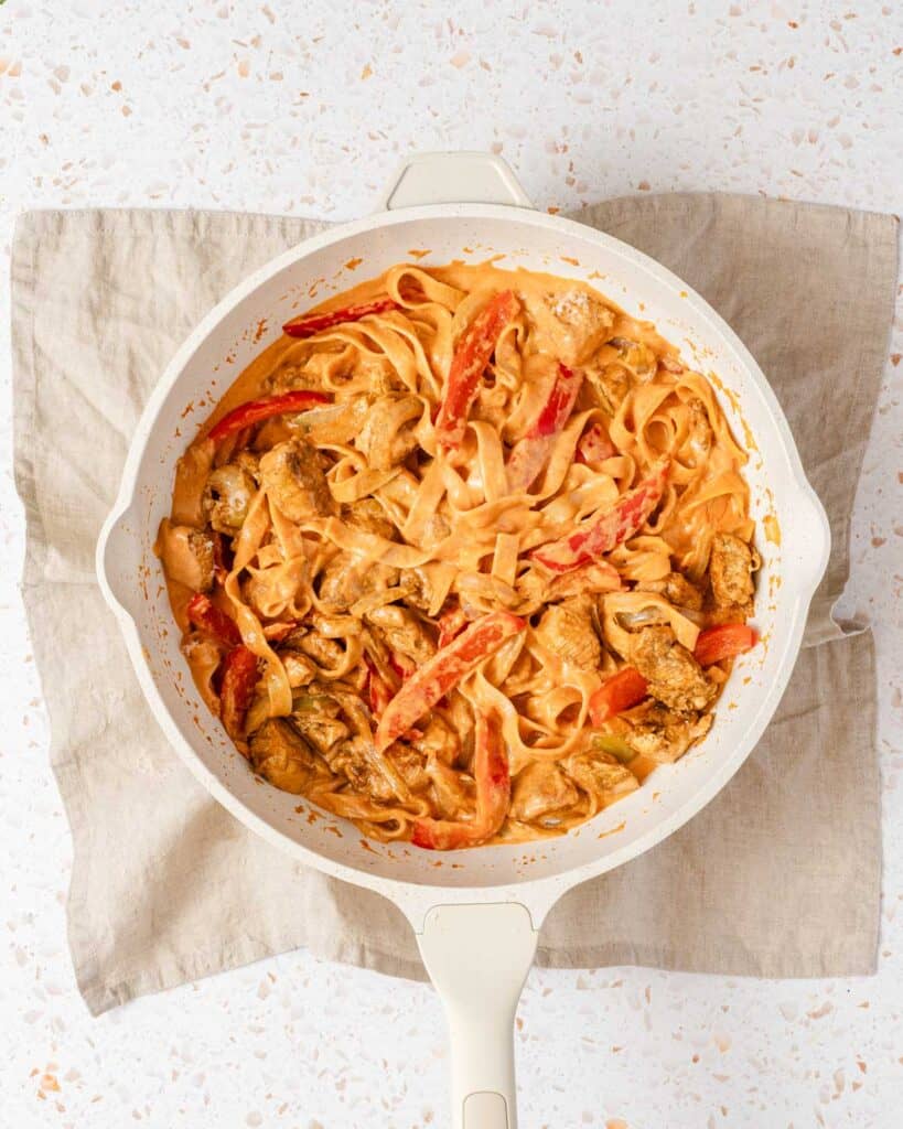 creamy Cajun pasta with chunks of chicken in white pan.