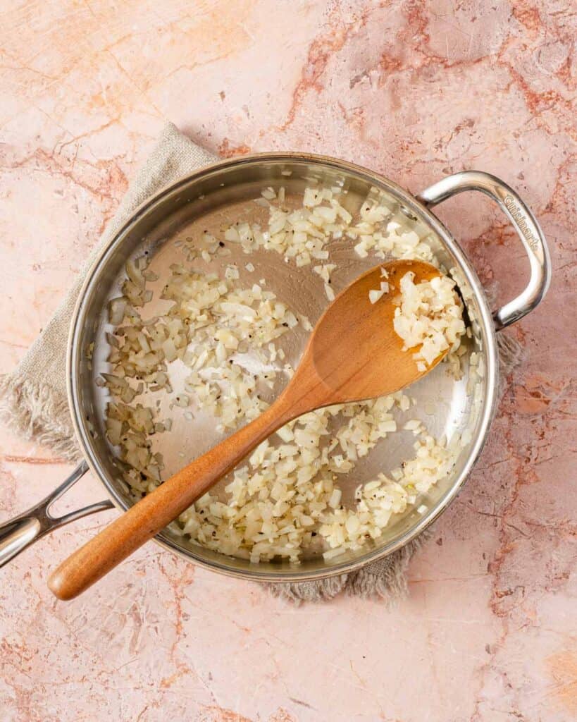 onion and garlic cooked in pan with wooden spoon.