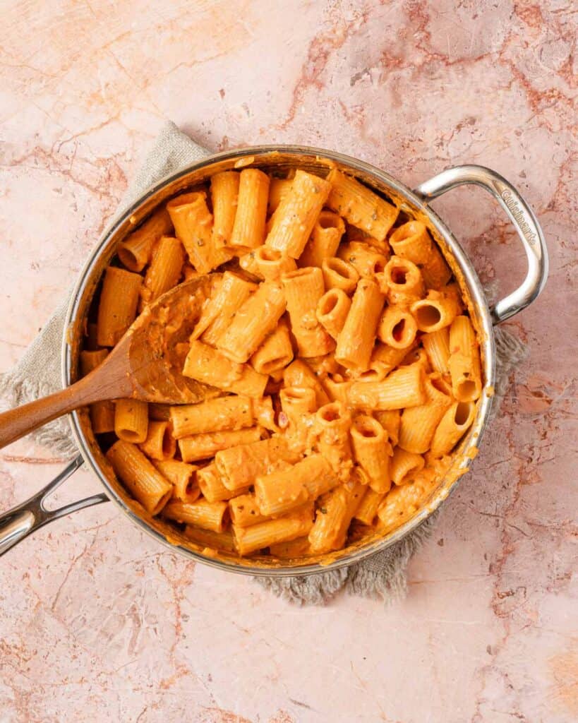 rigatoni tossed with creamy tomato sauce in pan with wooden spoon.