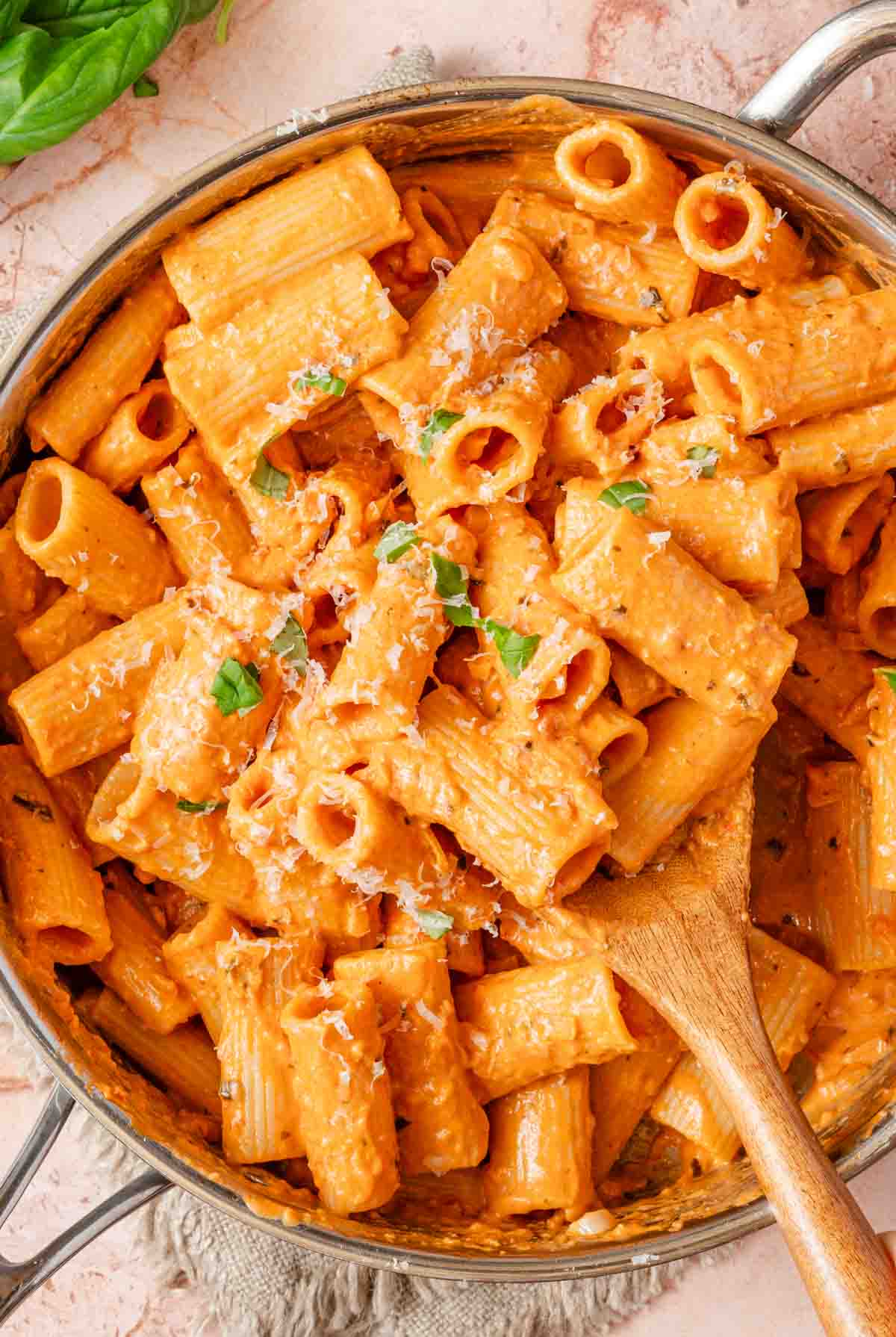 creamy pink pasta in pan with wooden spoon.