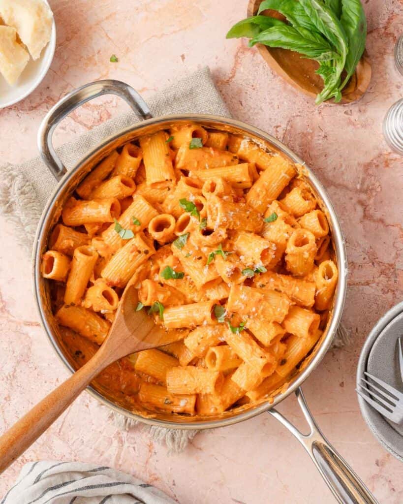 pink sauce pasta in pan with basil garnish.