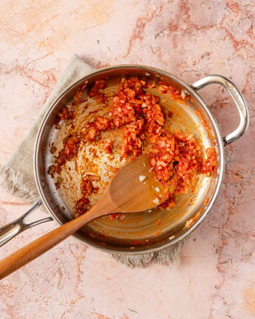 tomato paste and onions cooked in pan with wooden spoon.