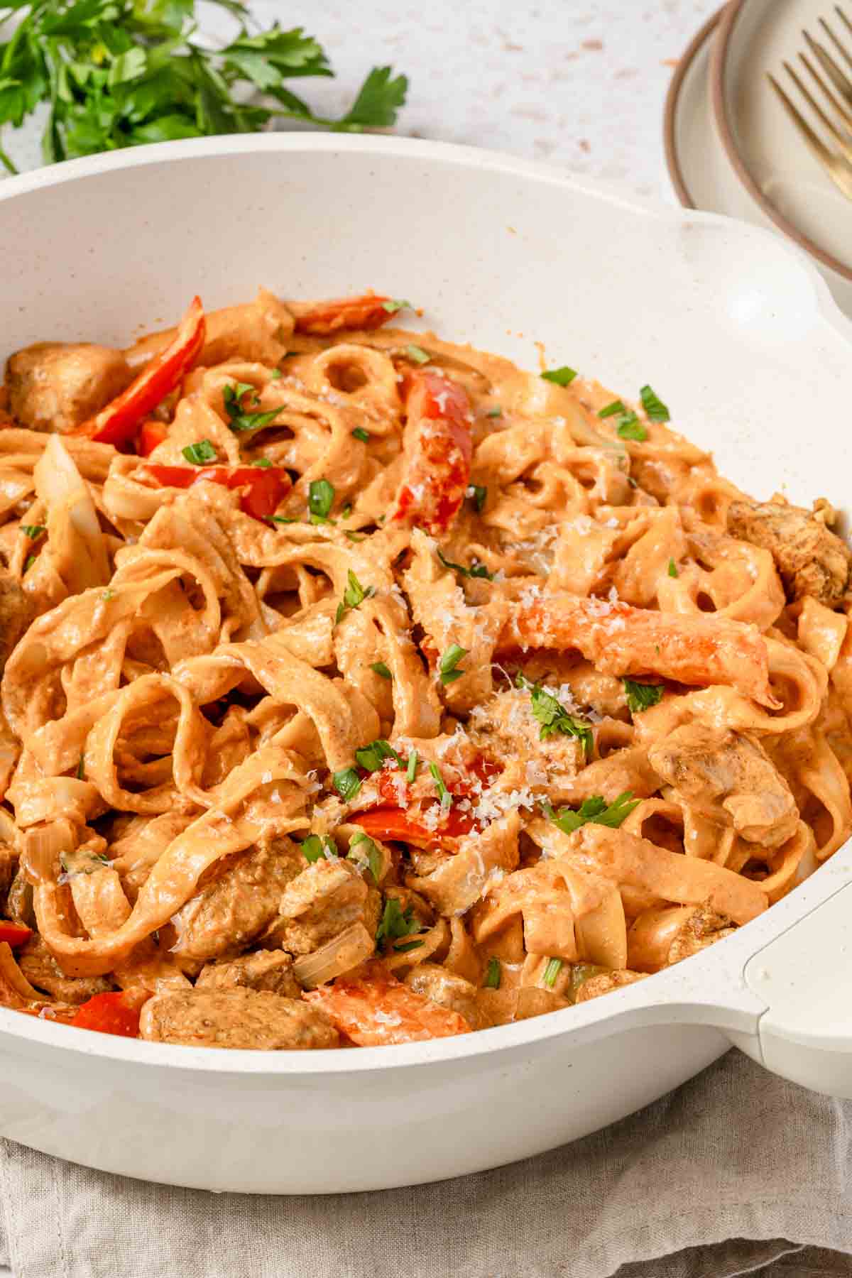 pot of creamy pasta with chunks of chicken and parsley on the side.